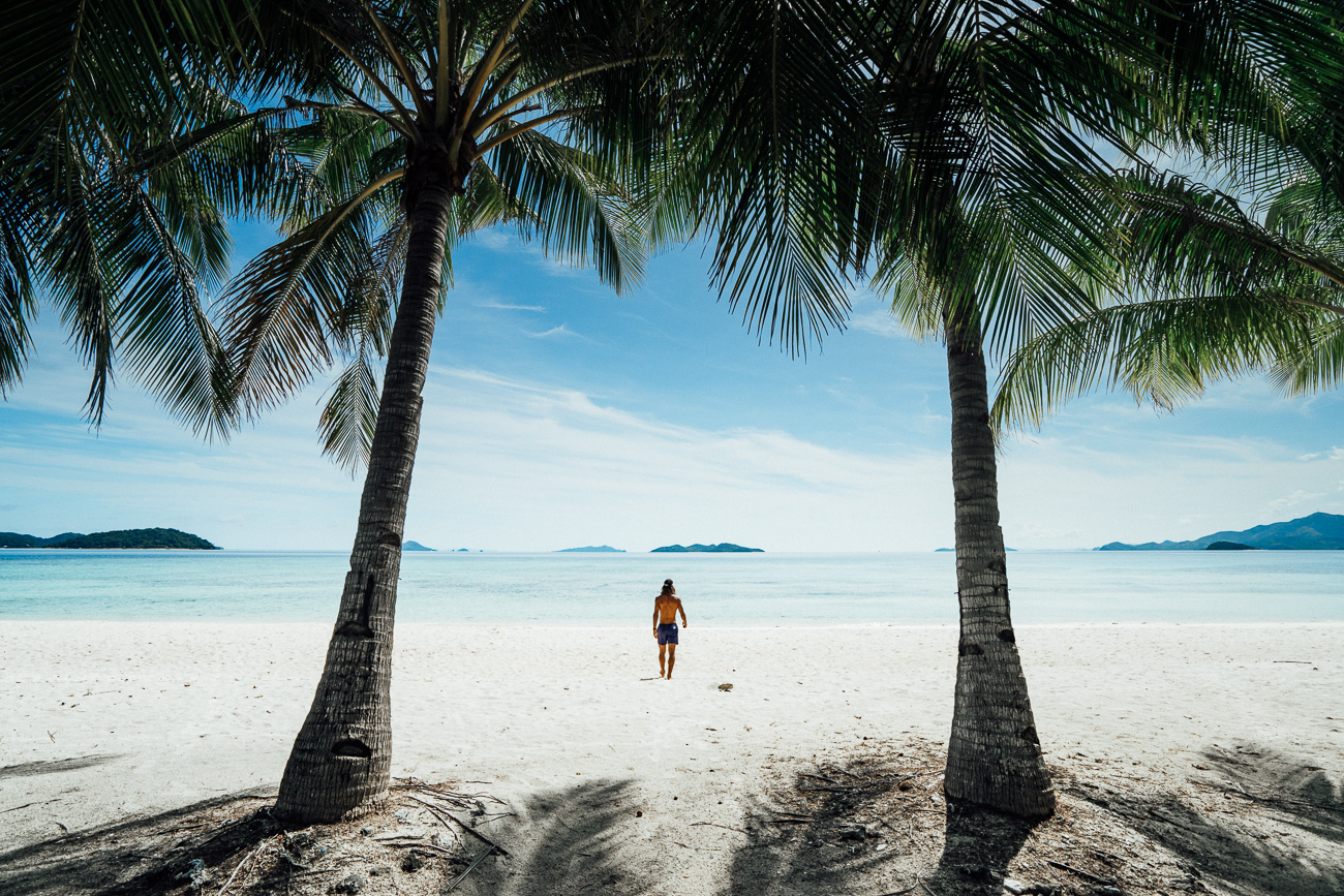 a woman walking on a beach between two palm trees.