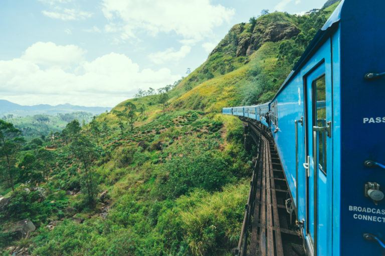 a blue train traveling through a lush green hillside.