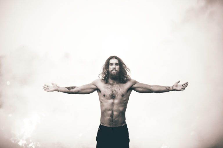 a man with long hair and a beard standing with his arms outstretched.