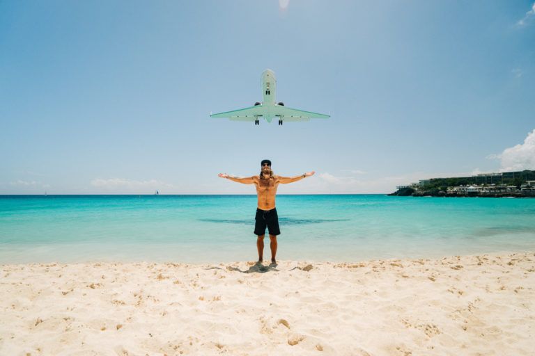 a man standing on the beach with his arms outstretched in front of an airplane.