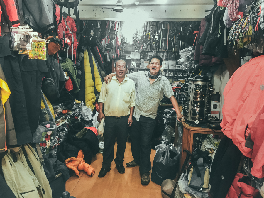two men standing in front of a store filled with clothes.