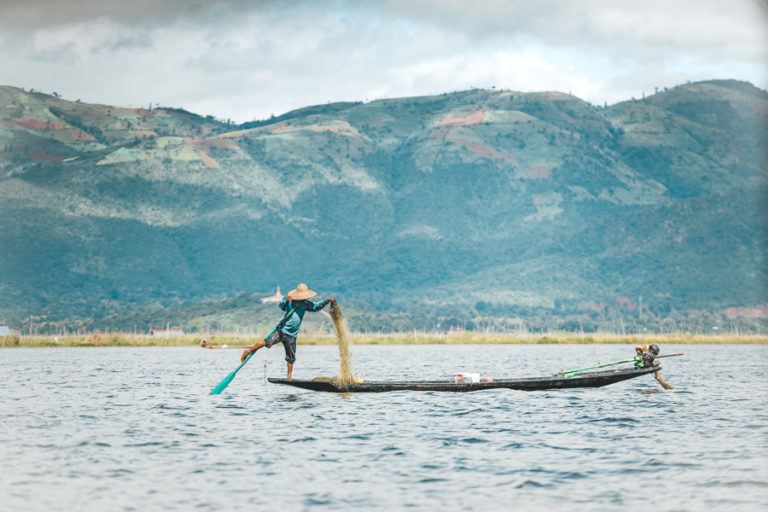 a man in a boat on a lake with mountains in the background.