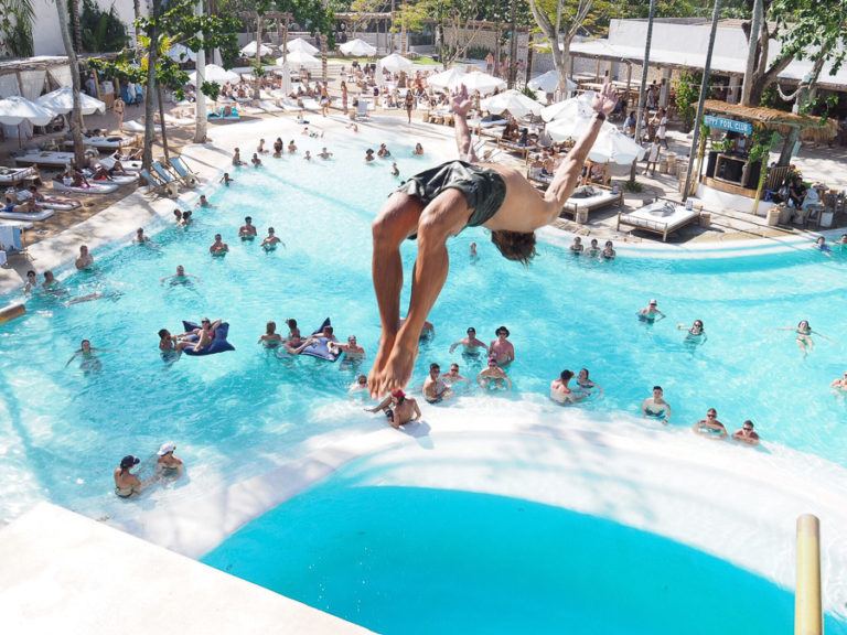 a man jumping into a pool with people in the background.