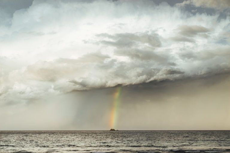 a rainbow appears in the sky over the ocean.
