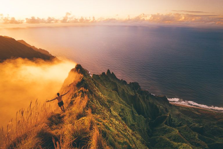 a person standing on top of a mountain next to the ocean.