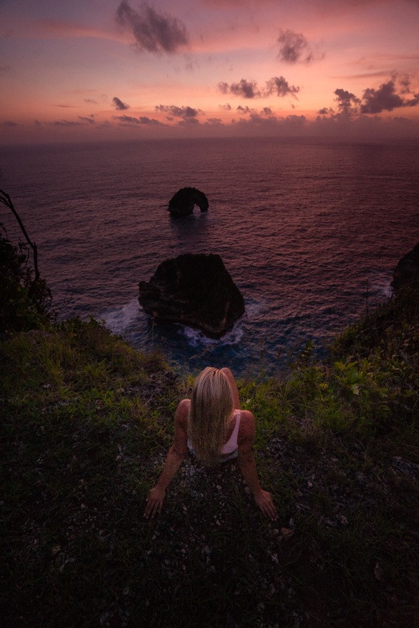 a woman sitting on a hill looking out at the ocean.
