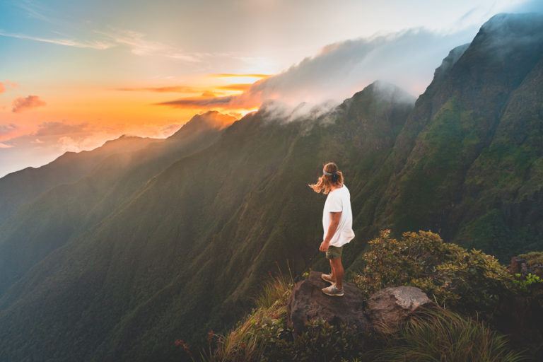 a woman standing on top of a mountain looking at a sunset.