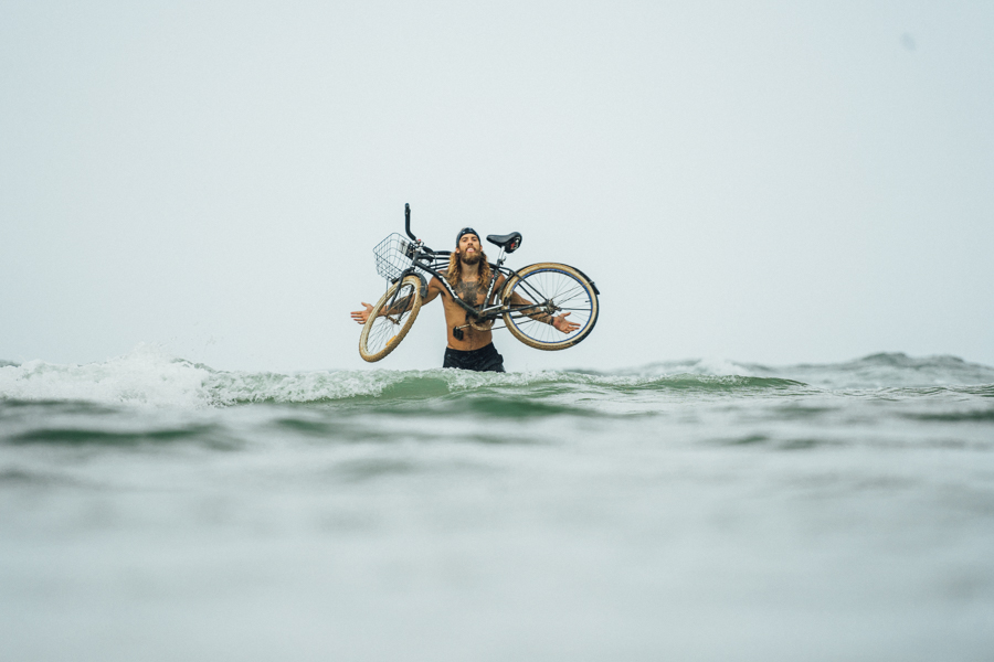 a man holding a bike in the ocean.