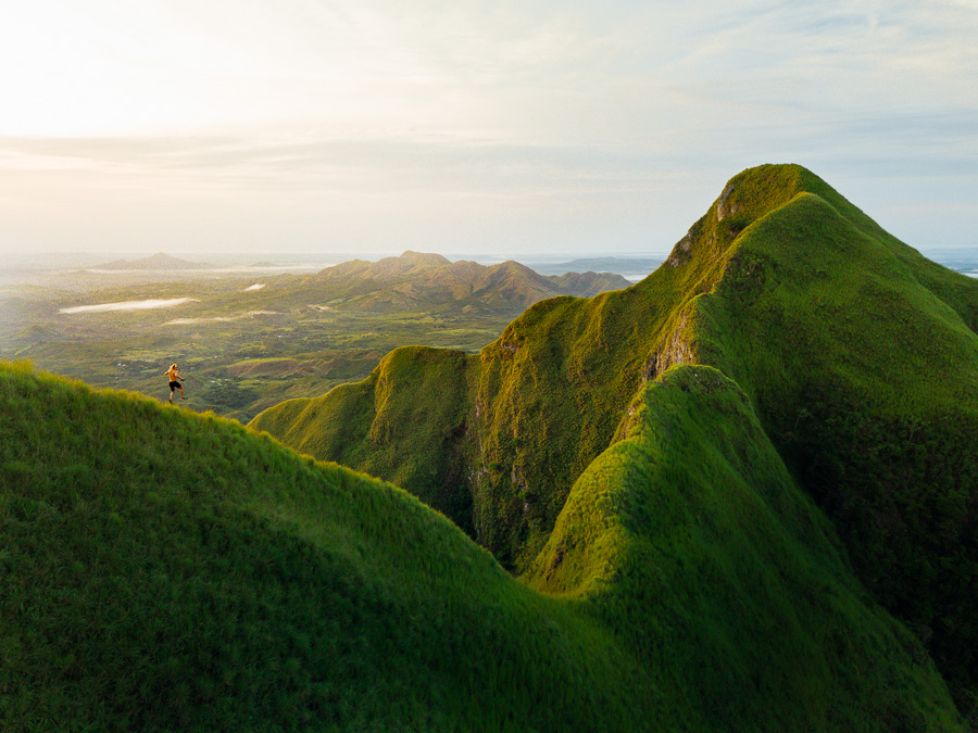 a person standing on top of a lush green mountain.