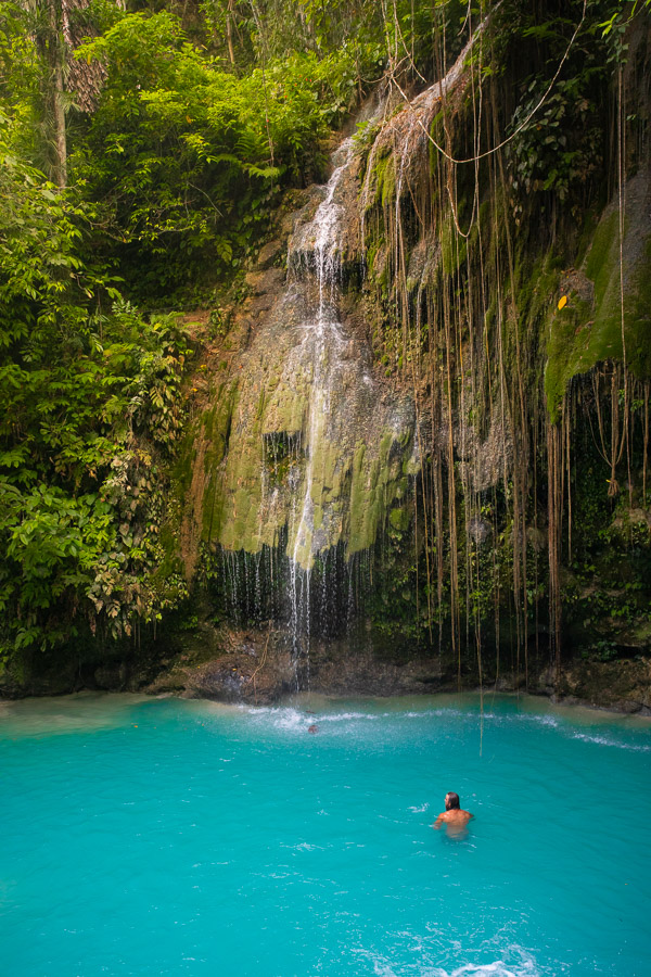 a person swimming in a pool in front of a waterfall.