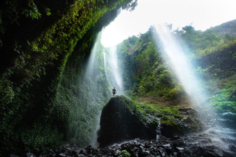 a person standing on a rock in front of a waterfall.