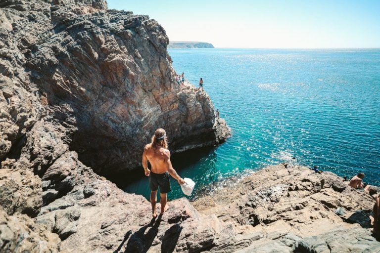 a man standing on top of a cliff next to the ocean.