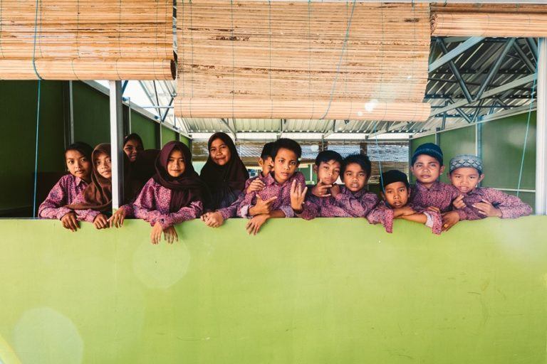a group of children standing behind a green wall.