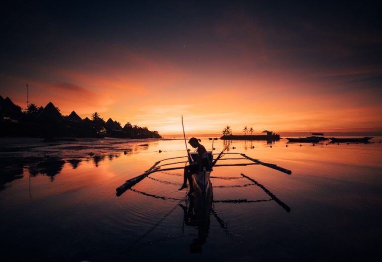 a man on a boat in the water at sunset.