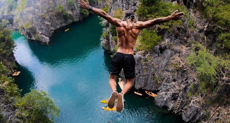 a man jumping off a cliff into a river.