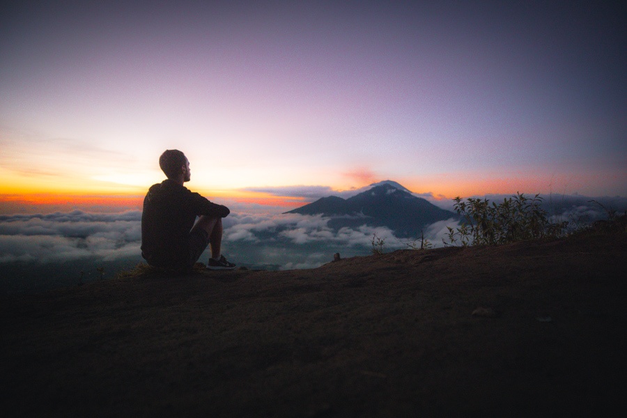 a man sitting on top of a mountain at sunset.