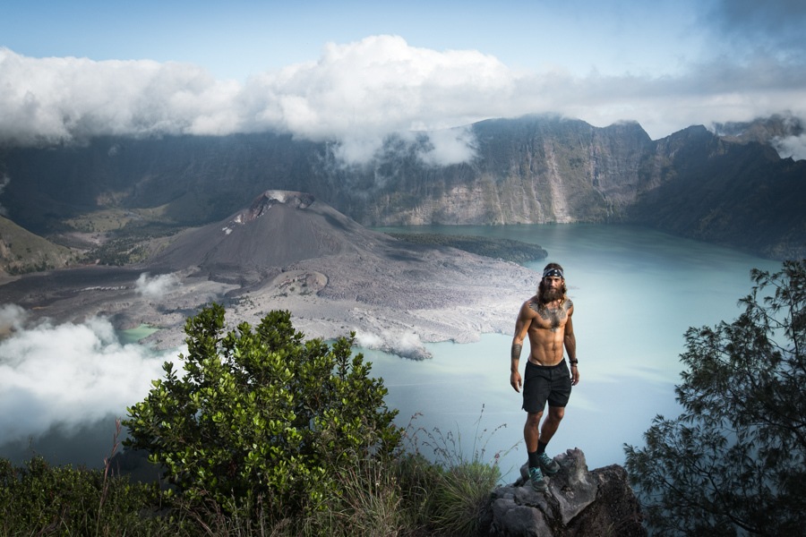 a man standing on top of a mountain next to a lake.
