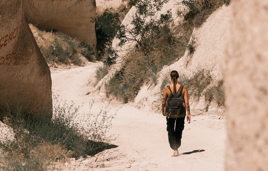 a woman walking down a dirt road in the desert.