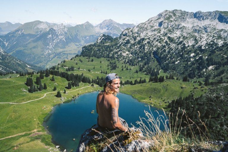 a man sitting on top of a mountain next to a lake.