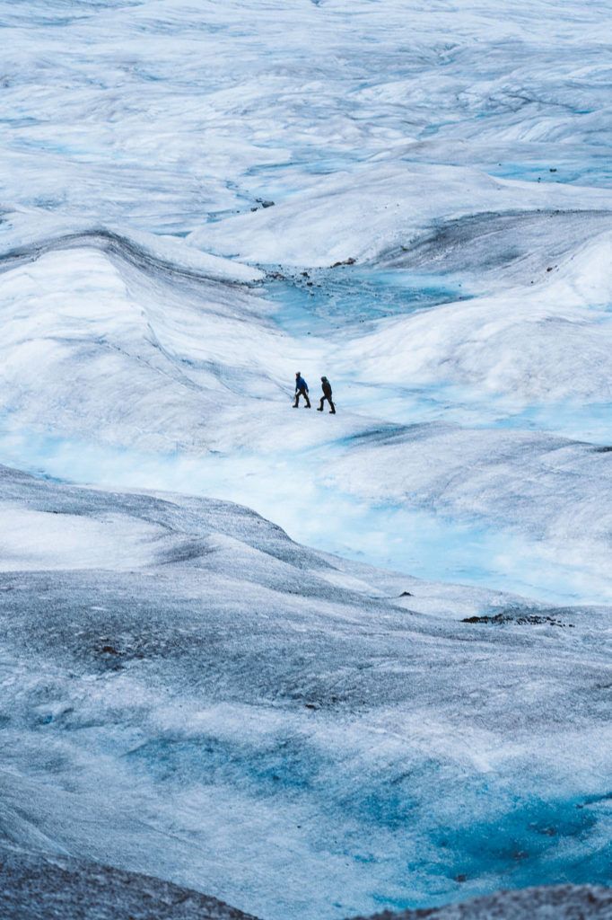 a couple of people walking across a snow covered field.