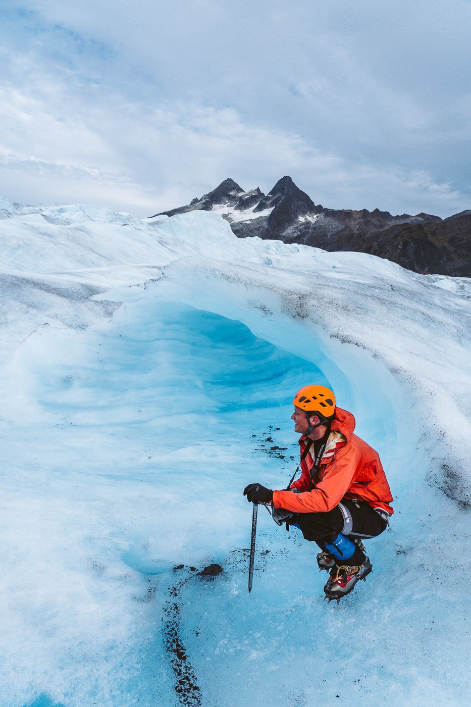 a man in an orange jacket on skis on a glacier.