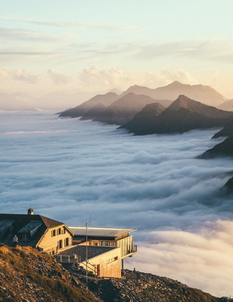 a house sitting on top of a mountain covered in clouds.