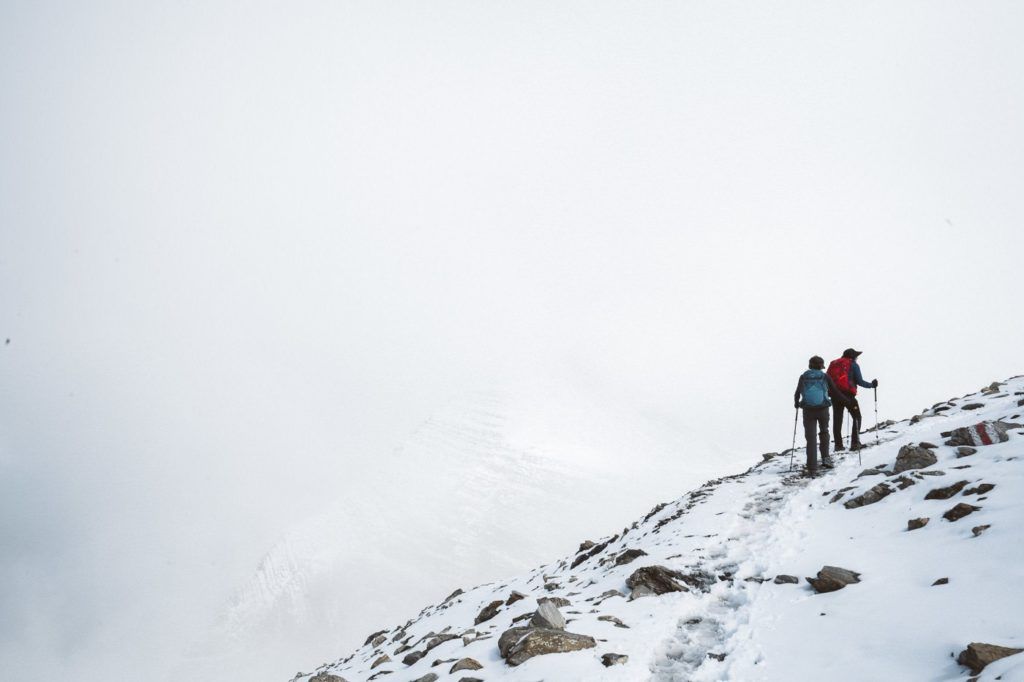 a couple of people walking up a snow covered mountain.