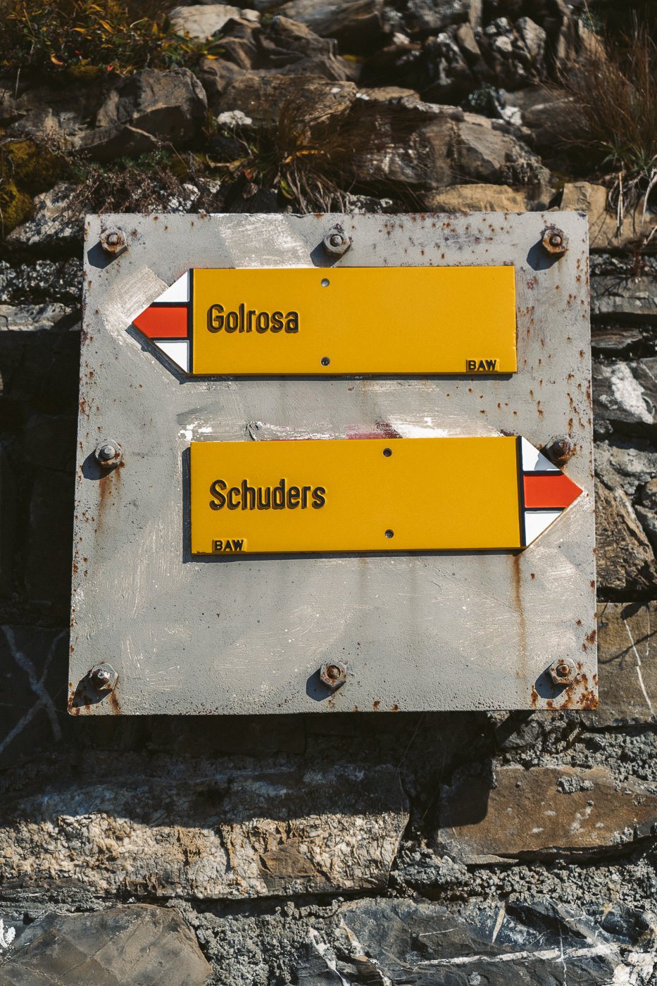 two signs on a stone wall pointing in opposite directions.