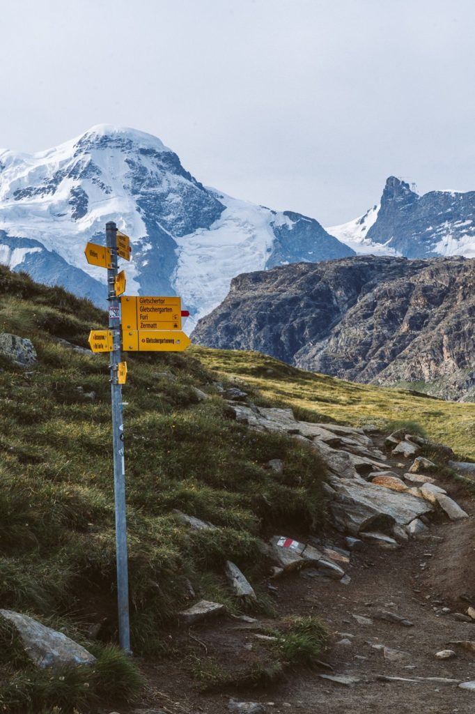 a yellow sign on a rocky trail with a mountain in the background.