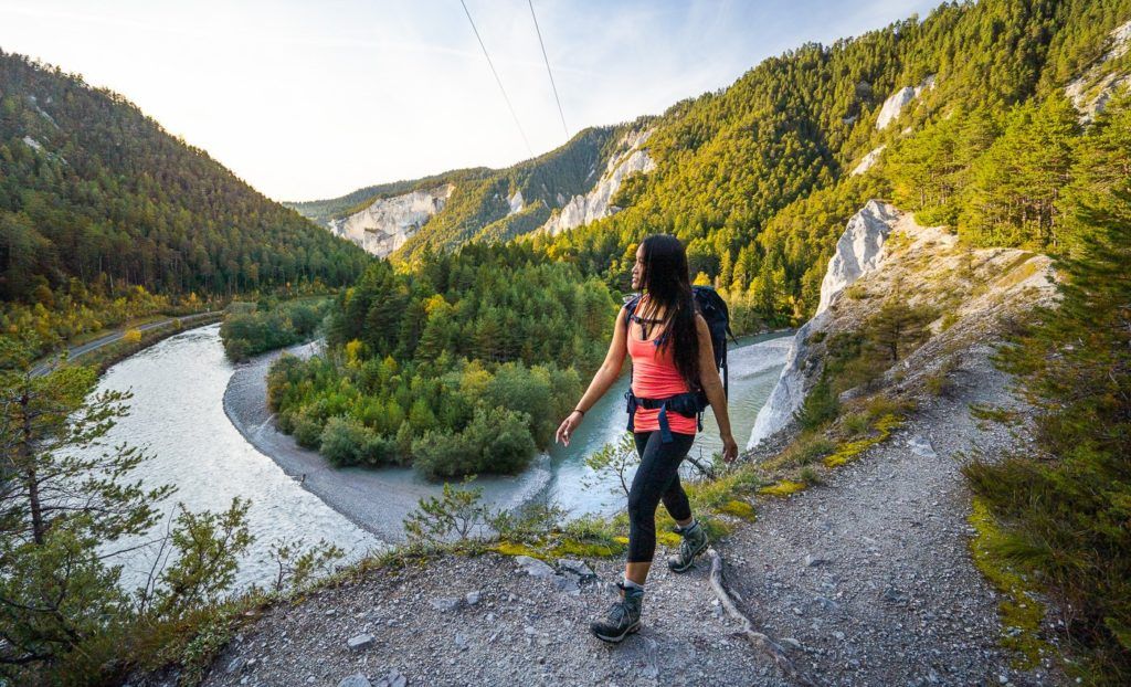 a woman with a backpack is standing on a cliff overlooking a river.