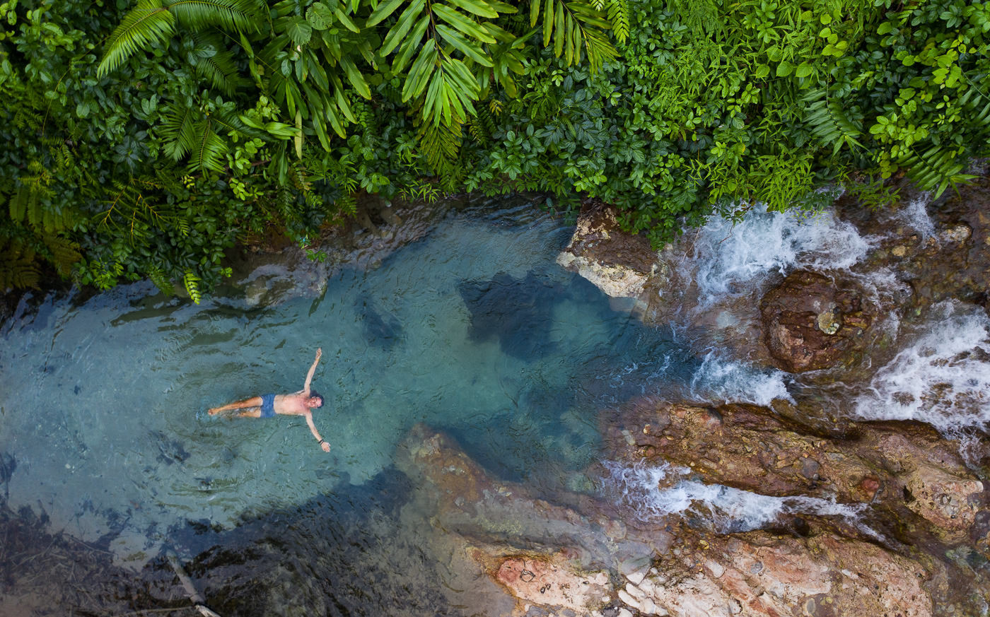 a person swimming in a river surrounded by trees.