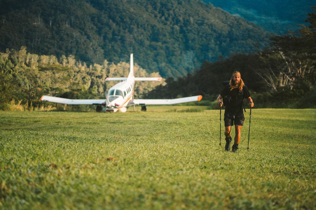 a woman walking across a lush green field next to a small airplane.