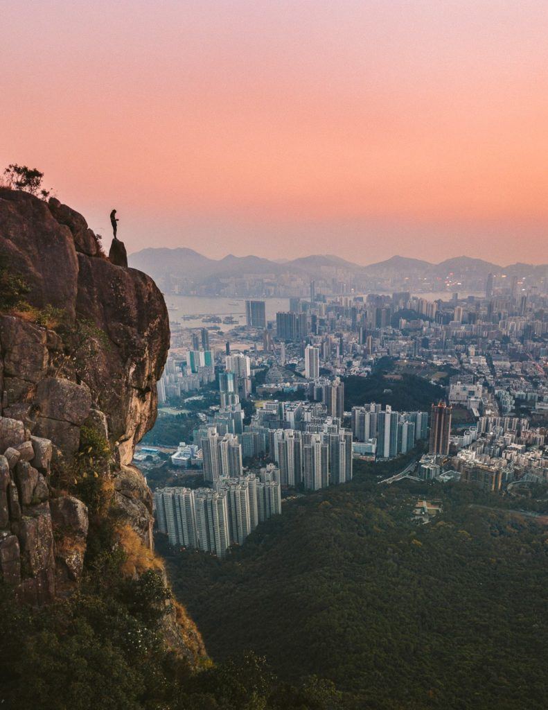 a person standing on top of a cliff overlooking a city.