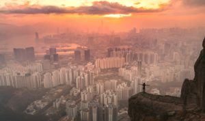 a person standing on top of a cliff overlooking a city.