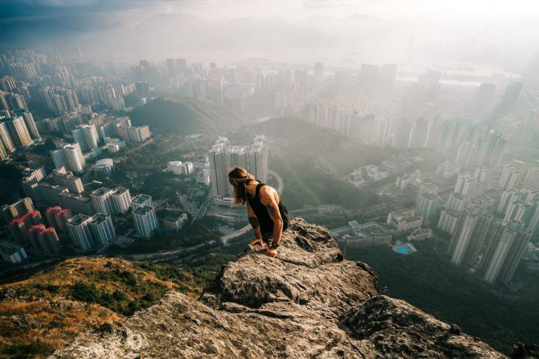 a woman standing on top of a mountain overlooking a city.