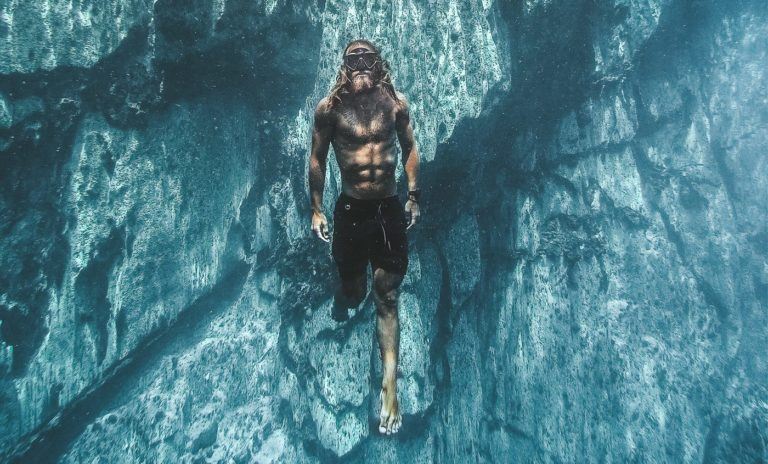 a man swimming in the ocean next to a cliff.