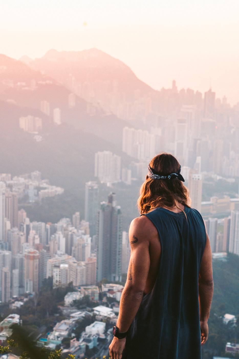 a man standing on top of a mountain looking at a city.