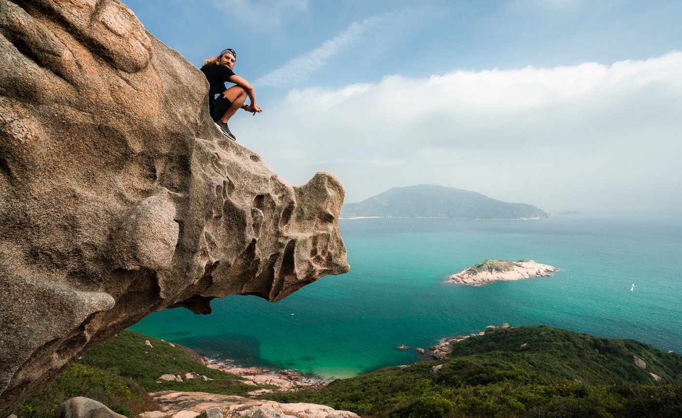 a man sitting on top of a rock next to the ocean.