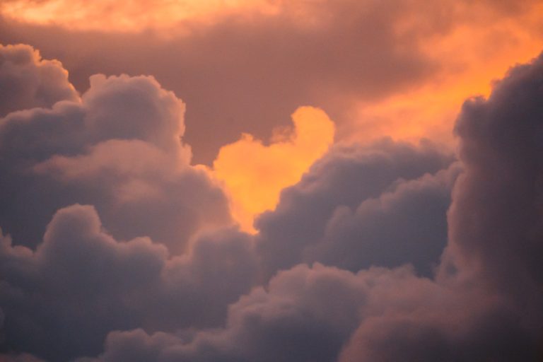 a plane flying through a cloudy sky at sunset.