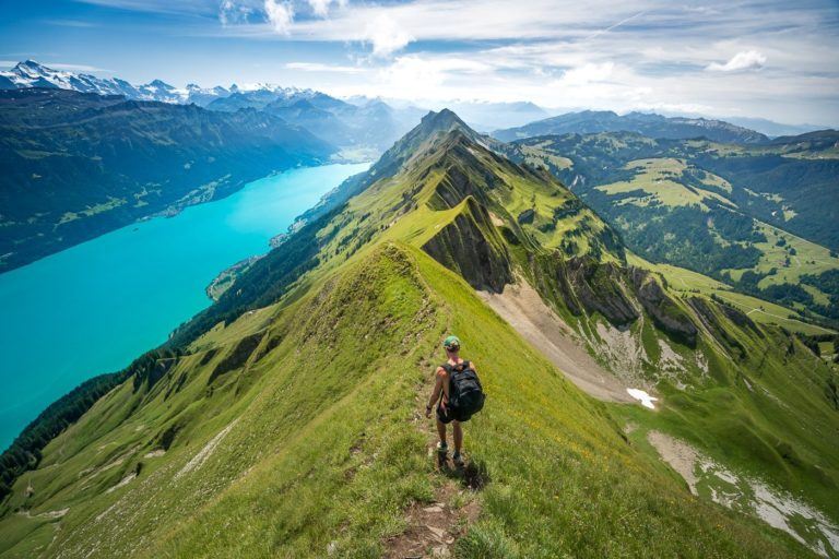 a man hiking up a steep mountain with a lake in the background.