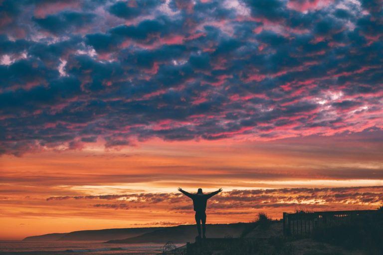a person standing on top of a cliff at sunset.