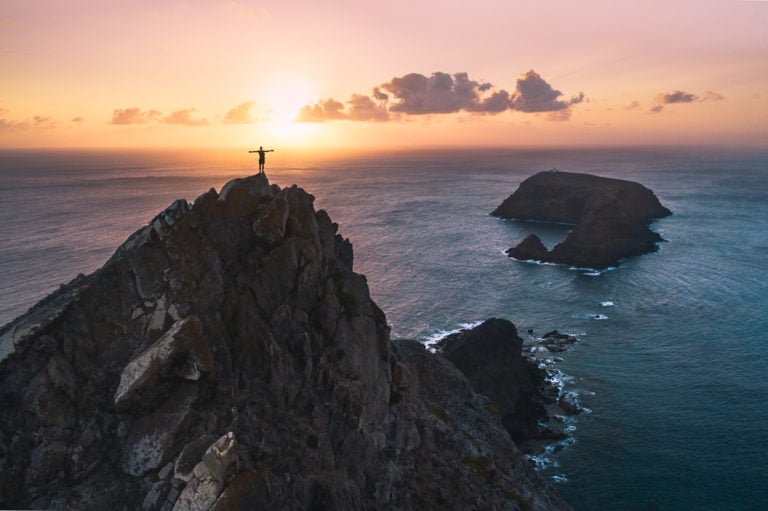 a person standing on top of a mountain next to the ocean.