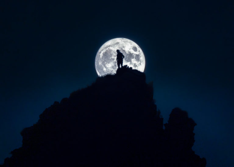 a person standing on top of a mountain under a full moon.