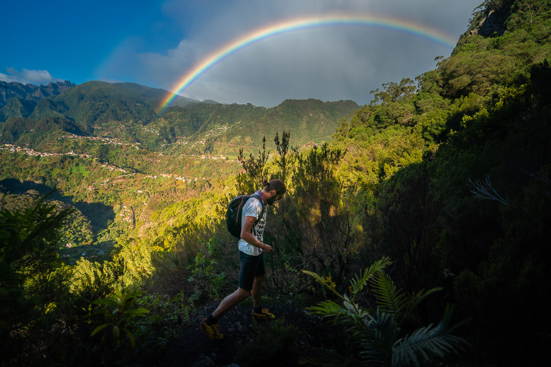 a man hiking up a mountain with a rainbow in the sky.