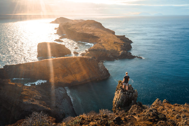 a person sitting on top of a cliff next to the ocean.
