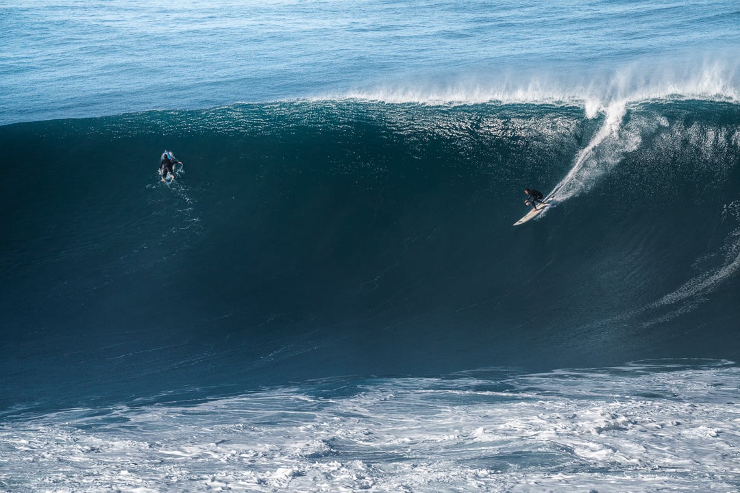 two surfers riding a large wave in the ocean.