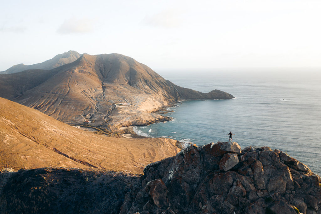 a person standing on top of a mountain next to the ocean.
