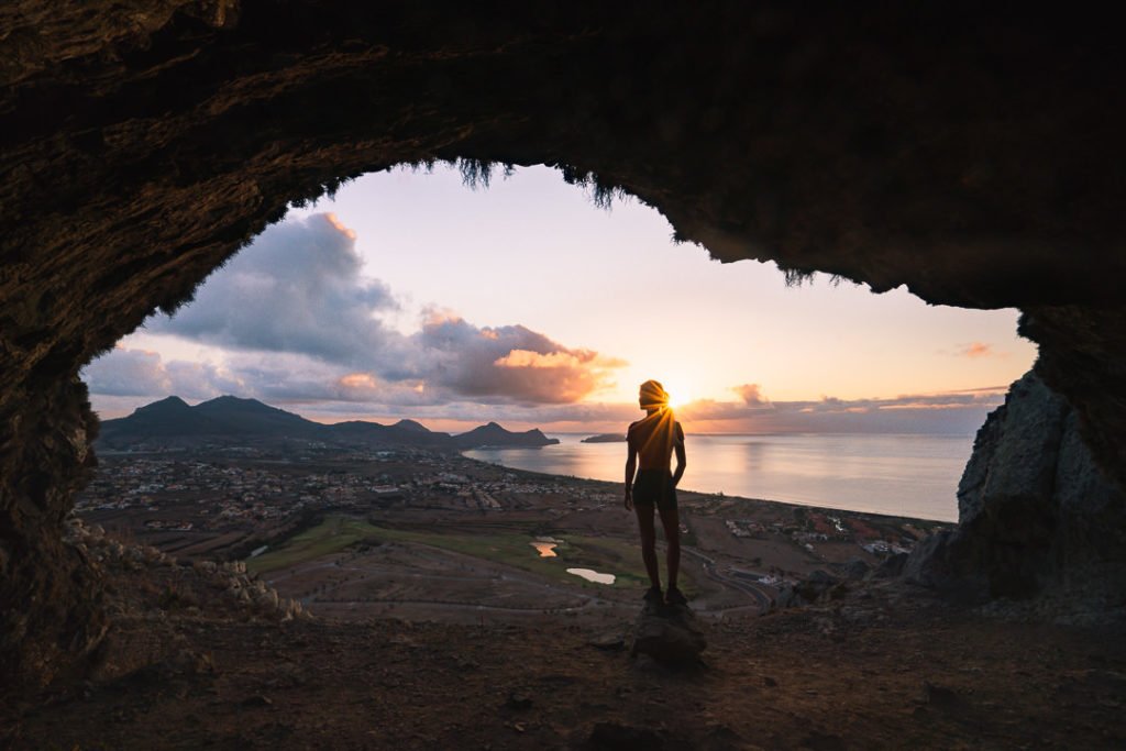 a person standing in a cave looking out at the ocean.