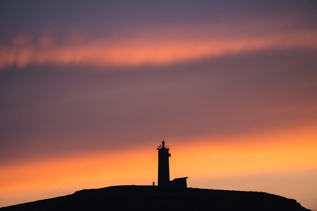 a lighthouse is silhouetted against a sunset sky.
