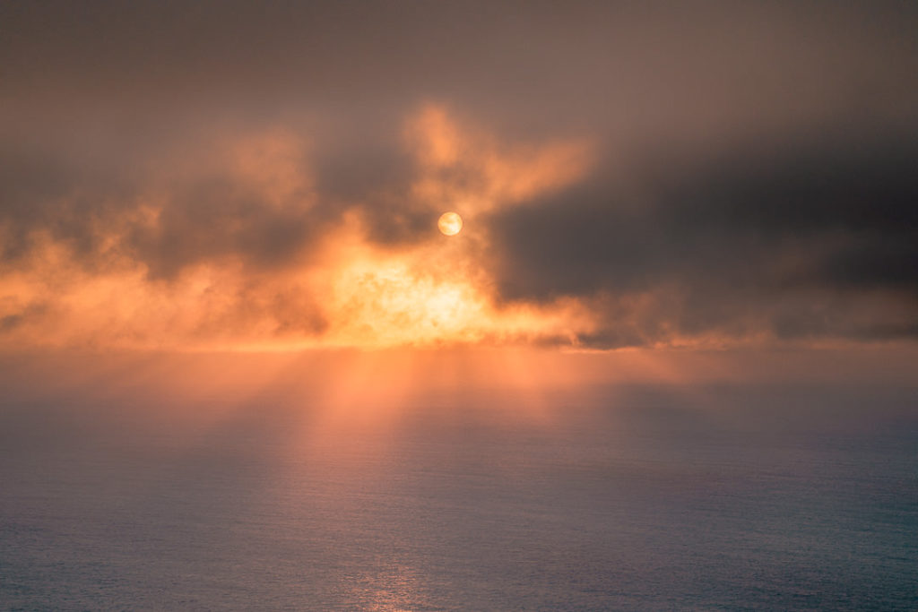 the sun is shining through the clouds over the ocean.